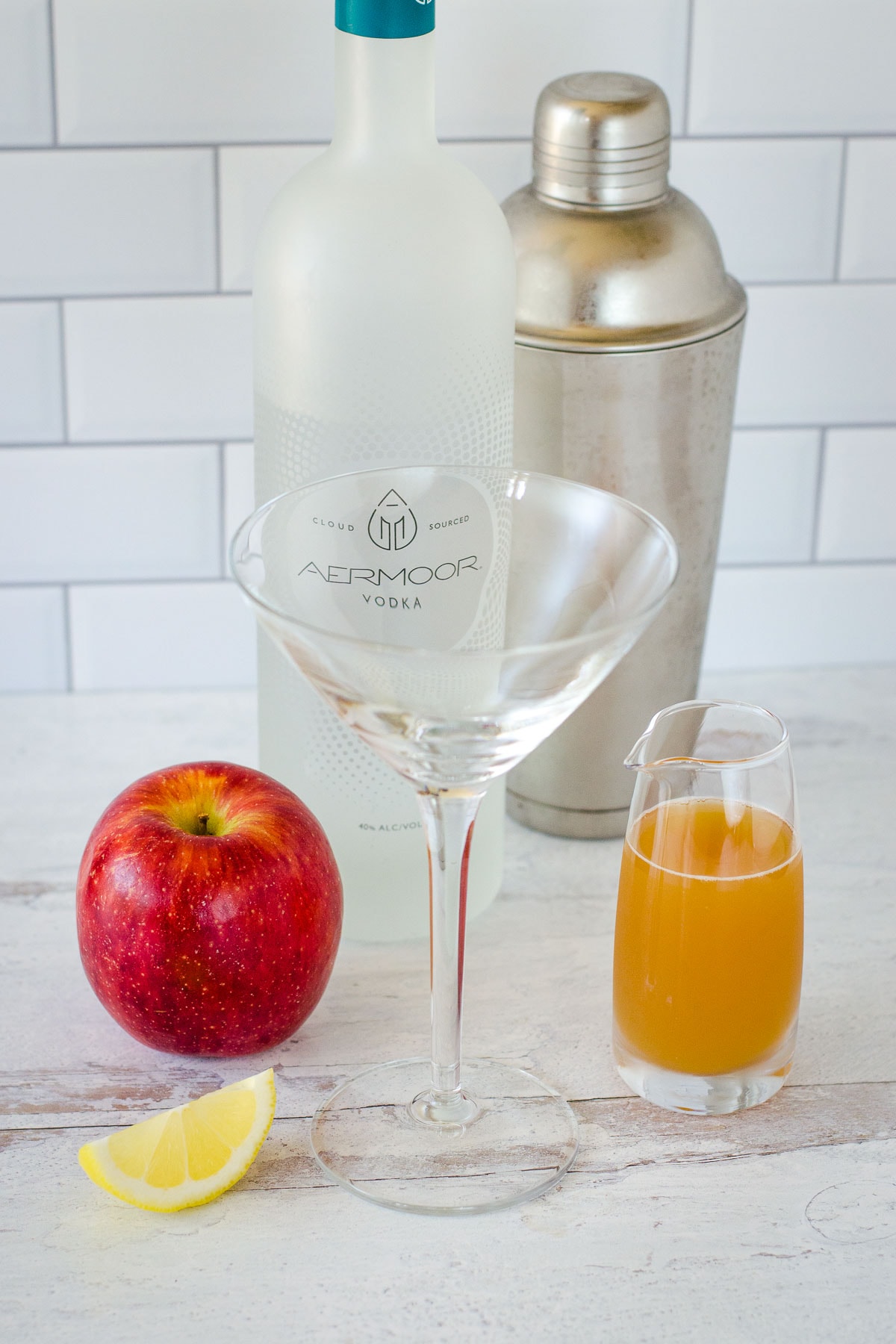 Lemon wedge, apple, vodka, cocktail shaker, apple cider and martini glass.