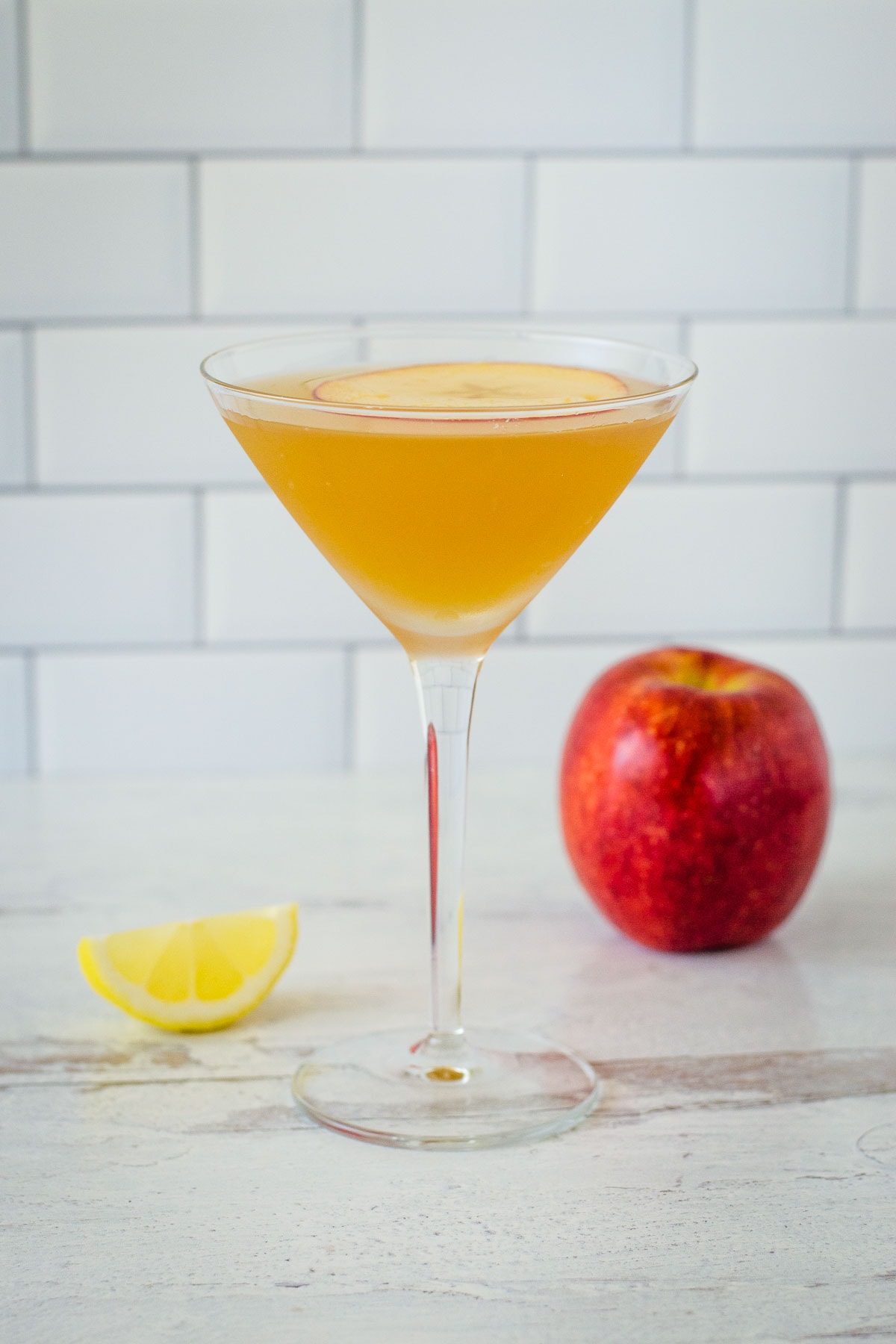 Apple cider martini with lemon wedge and apple in background.