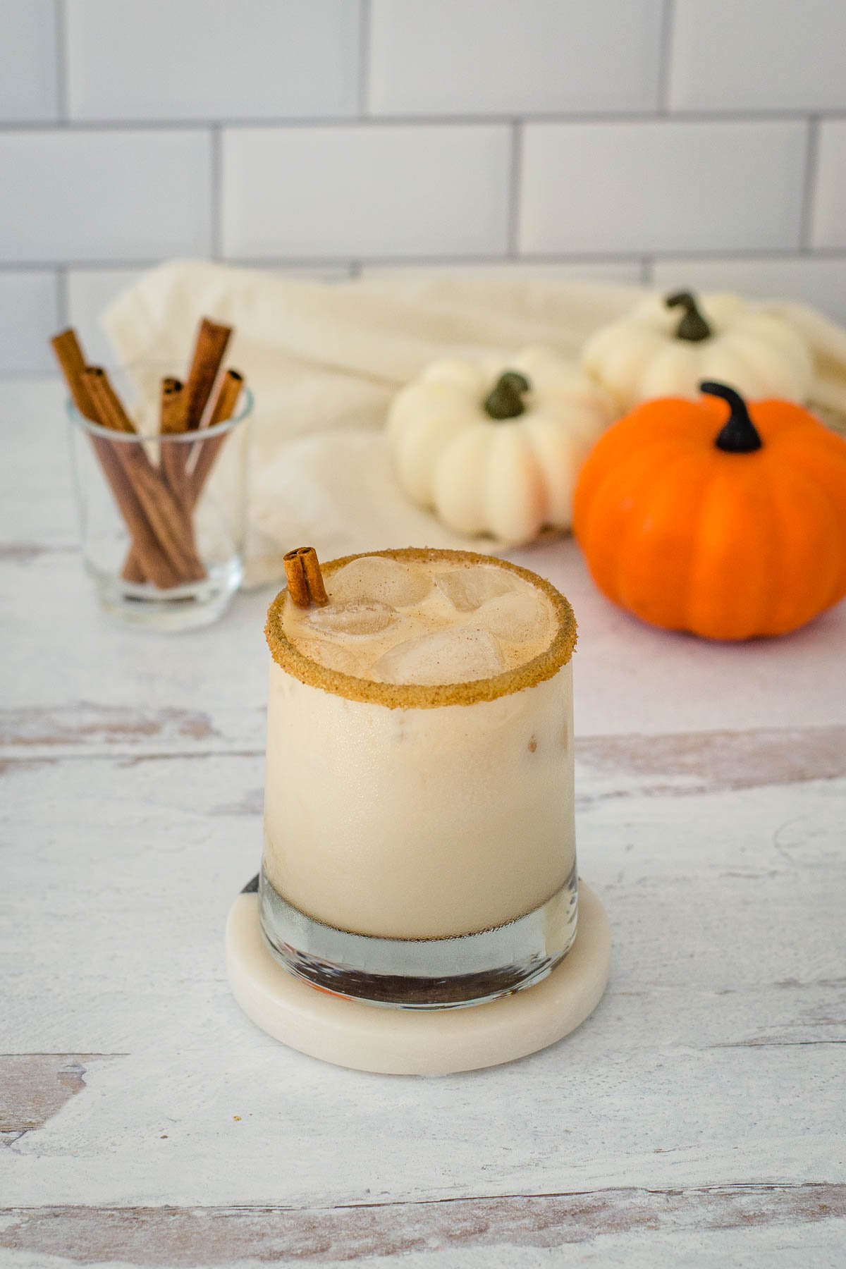 Pumpkin spice white Russian cocktail with cinnamon sticks and mini pumpkins in the background.