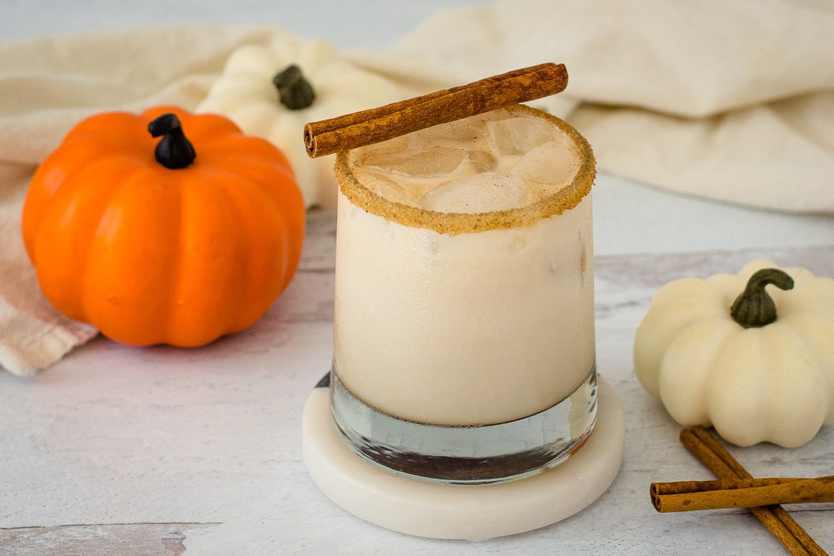 Pumpkin spice white Russian cocktail with cinnamon sticks and mini pumpkins in the background.