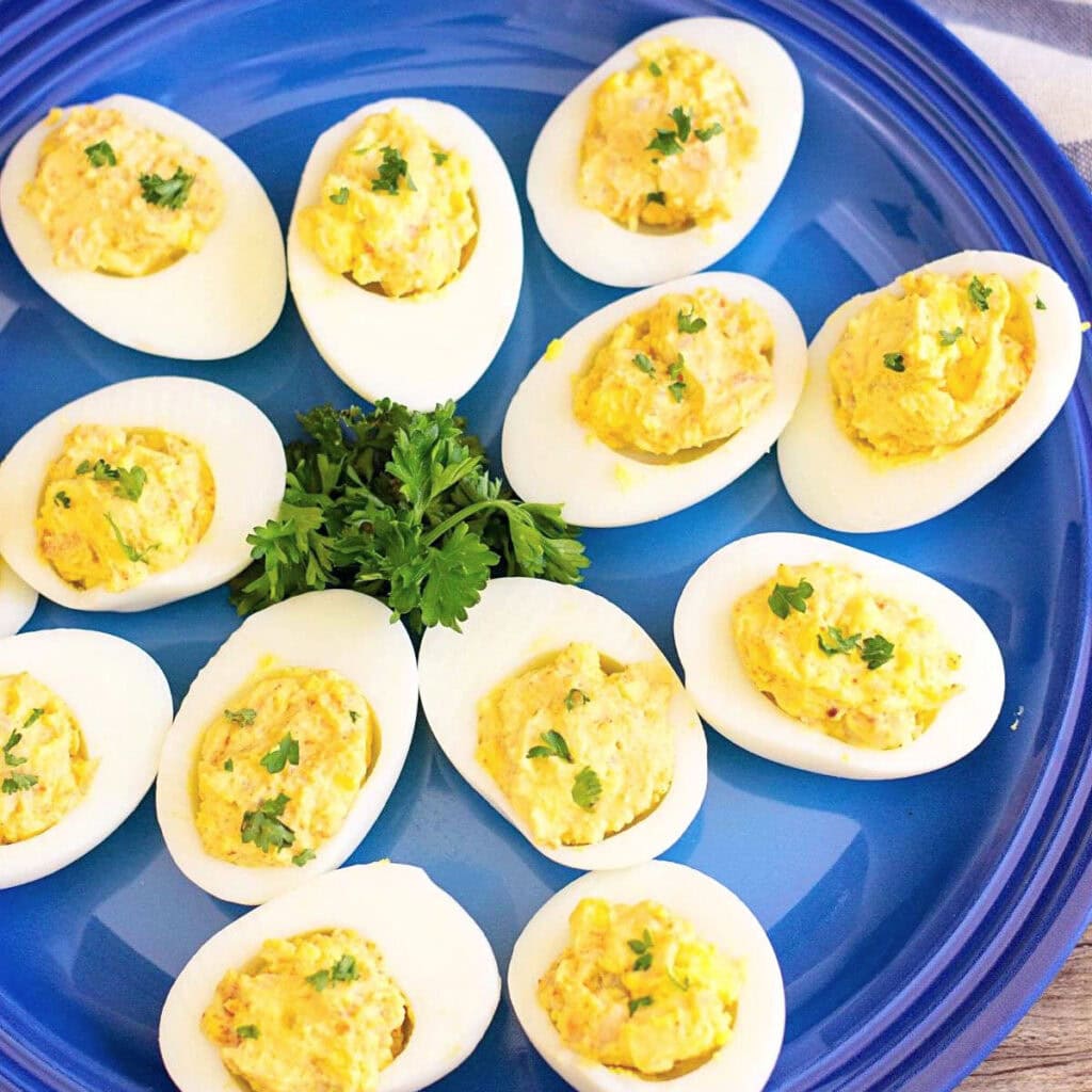Shrimp deviled eggs with herbs on blue plate.