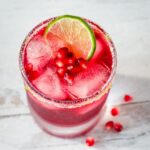 Pomegranate margarita with lime salt rim, lime slice and pomegranate arils.