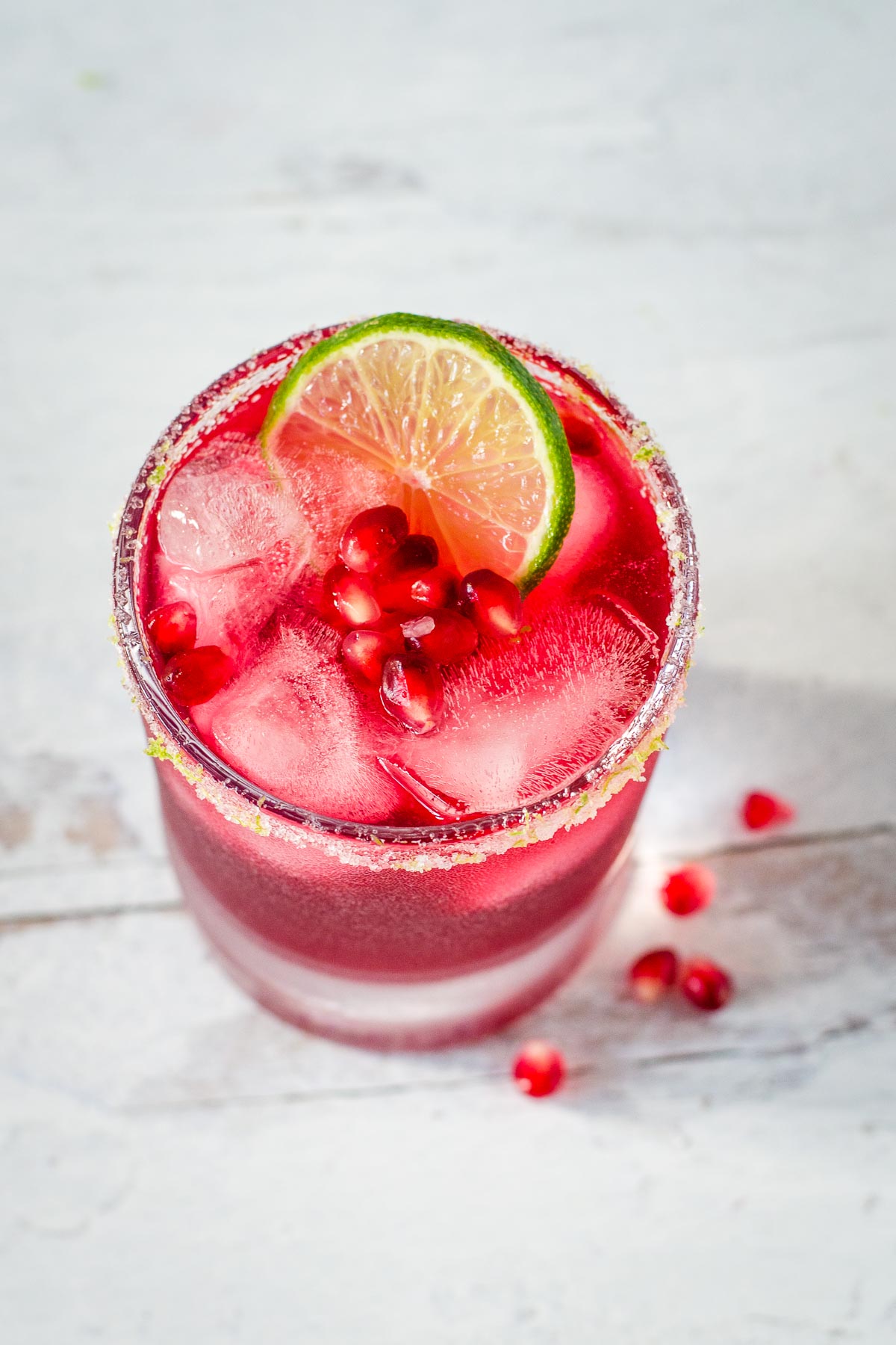 Pomegranate margarita with lime salt rim, lime slice and pomegranate arils.