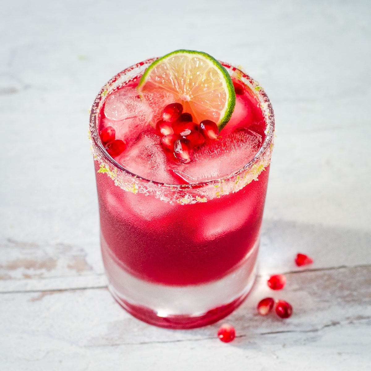 Pomegranate margarita with lime salt rim, lime slice and pomegranate arils.