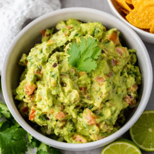 Bowl of guacamole with tomatoes, cilantro, lime and tortilla chips.