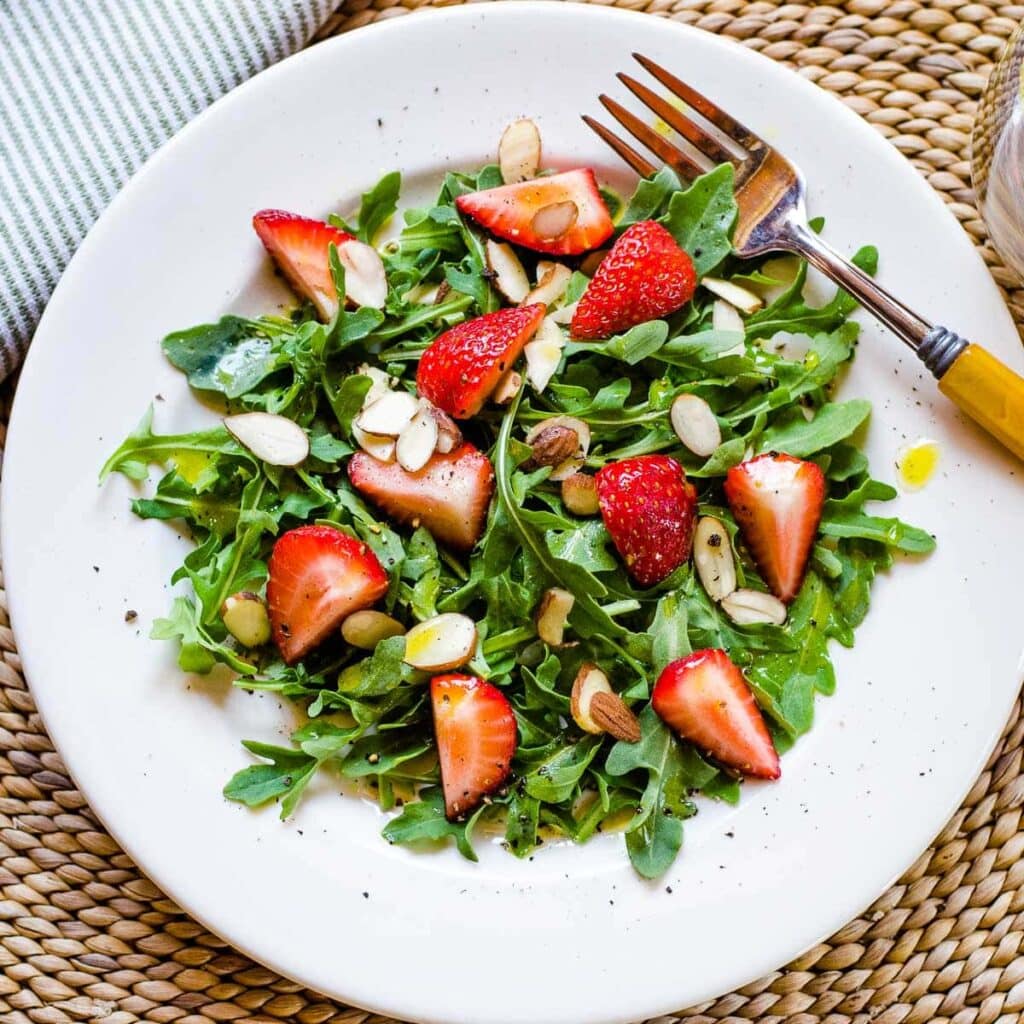 Strawberry arugula salad with almonds and lemon dressing on plate with fork.