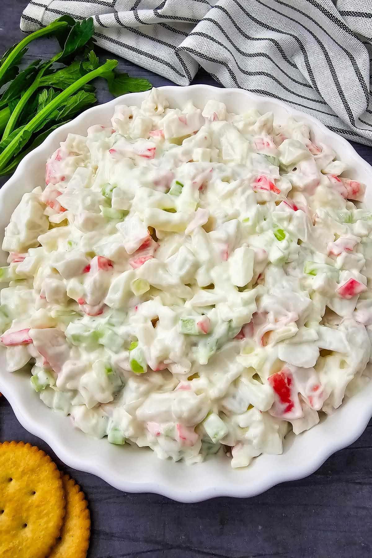 Crab salad in white dish next to crackers, celery stalks and napkin.