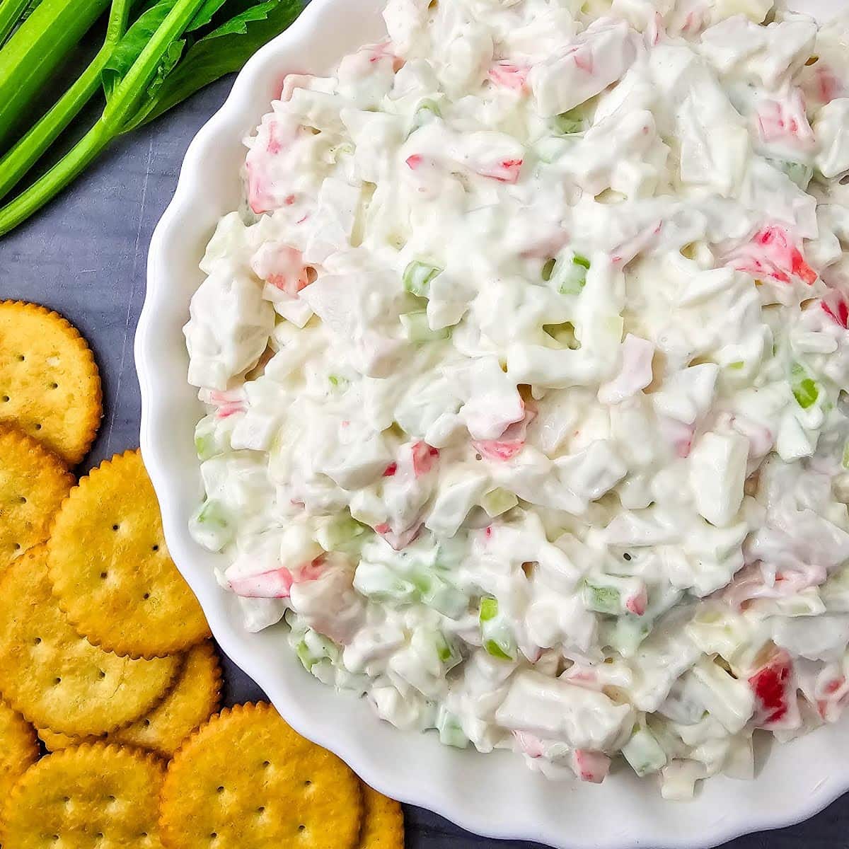Crab salad in white dish with celery and crackers.