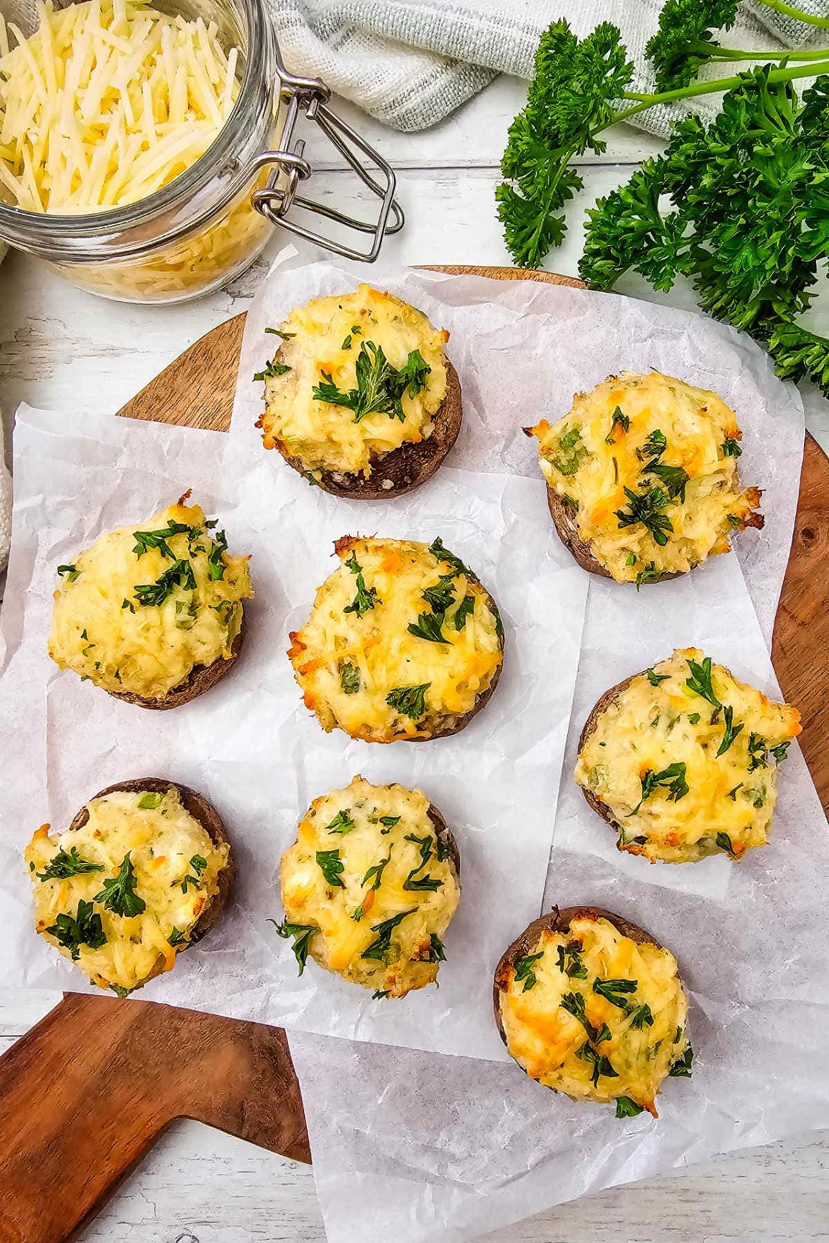 Crab stuffed mushrooms with melted cheese on top arranged on wood board with parchment paper.