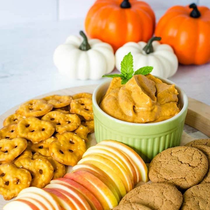 Pumpkin cream cheese dip with pretzels, apple slices, ginger snaps and pumpkins in the background.